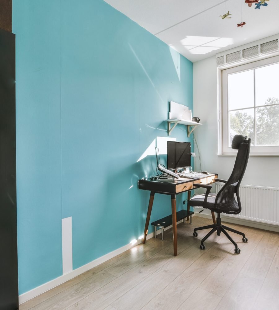 Comfortable chair placed near table with computer monitors against blank whiteboard and mirror in light home office in contemporary flat