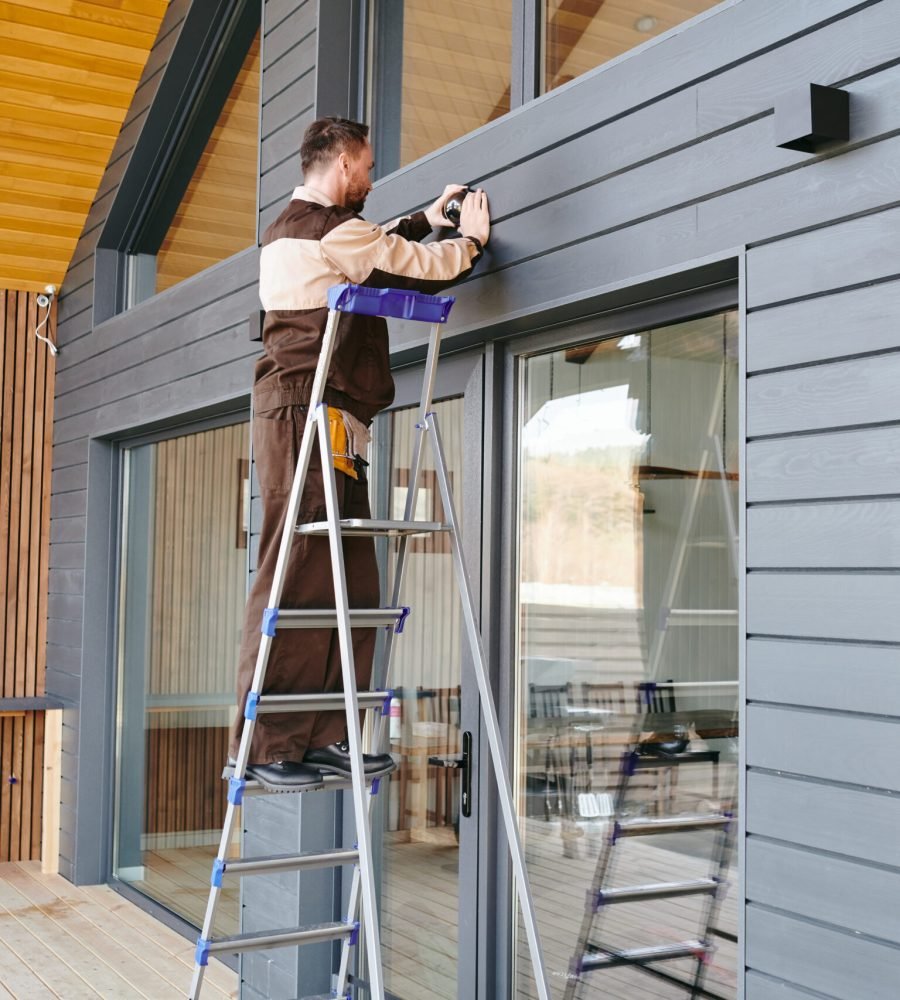 Young worker putting alarm system on wall over large door of house