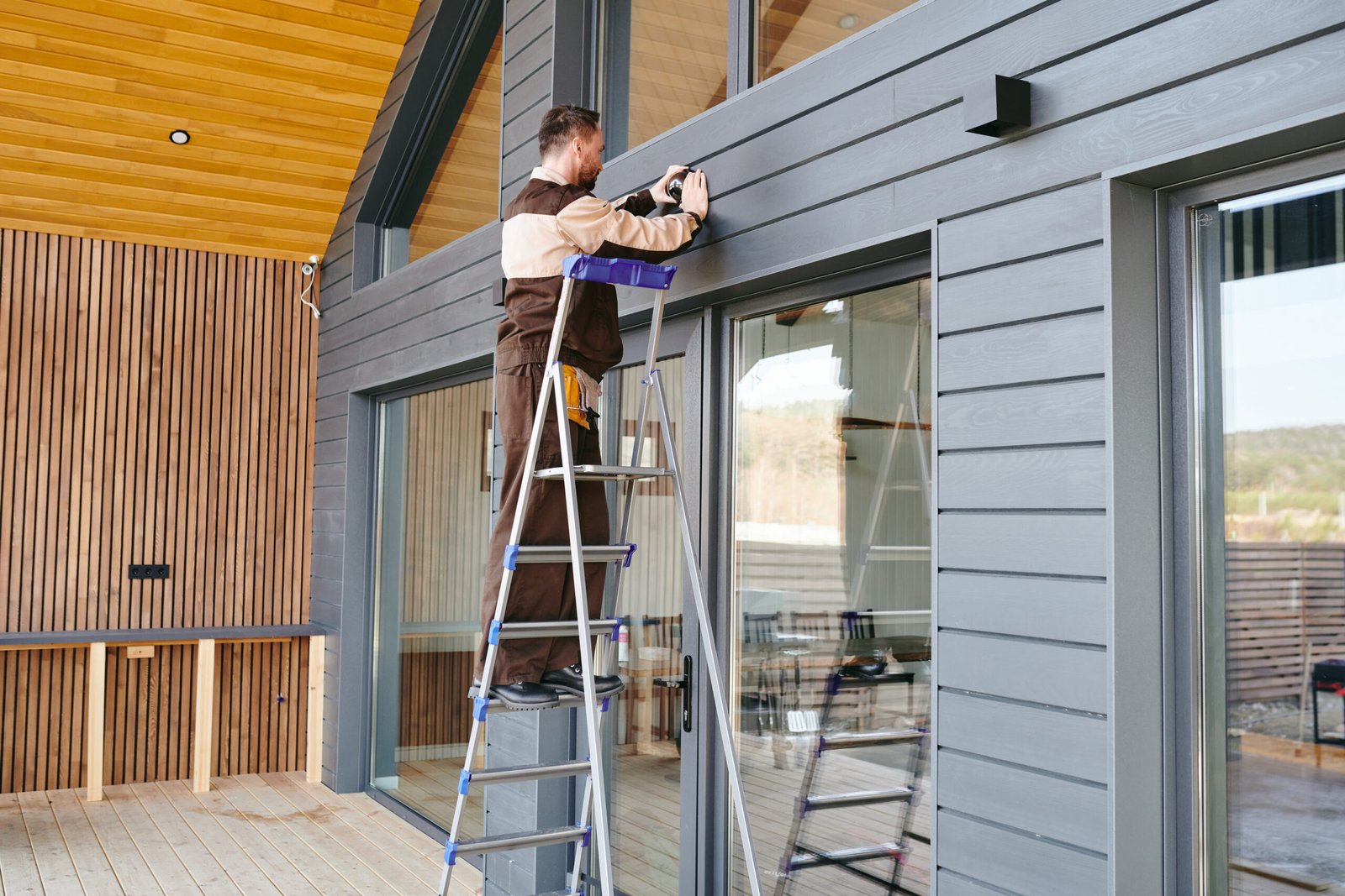 Young worker putting alarm system on wall over large door of house
